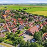 Dorf mit roten Dächern, umgeben von grünen Feldern und einem Fluss.