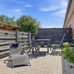 Terrasse mit Sitzgelegenheiten, Holzumrandung und Pflanzen. Hintergrund: Haus und Bäume.