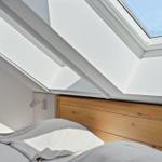 Schlafzimmer mit Holzkopfteil und Dachfenster. Bett mit weißen und grauen Kissen.