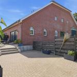Roter Backsteinbau mit Terrasse und Holzzaun. Pflanzkübel und Sitzgelegenheiten.