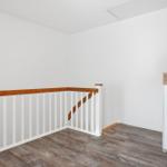 Helle Etage mit Holzgeländer und Holzboden. An der Wand steht ein weißer Schrank.