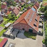 Roter Backsteinbau mit Solaranlage und großem Hof. Umgeben von grüner Landschaft und Nachbarhäusern.