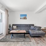 Wohnzimmer mit grauem Sofa, Holztisch und Treppe zur oberen Etage.