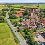 Aerial view of a village with red-roofed houses, green fields, and a road running through.