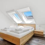Schlafzimmer mit Dachfenstern, Holzbett und Nachttisch.
