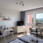 Zimmer mit Bett, Esstisch, TV und Balkon mit Blick auf Gebäude.