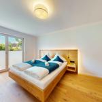 Schlafzimmer mit Holzbett, Fenster und blauer Bettwäsche.