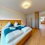 Schlafzimmer mit Holzbett, Kleiderschrank und Blick in die Badewanne.