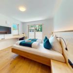 Schlafzimmer mit Bett, TV und Fenster. Holzboden und Wandgestaltung.
