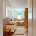 Badezimmer mit Badewanne, Waschbecken und Spiegel. Holzakzent und Teppich.
