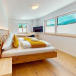 Schlafzimmer mit Holzbett, Fenstern und Fernseher
