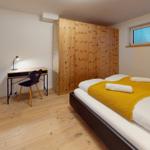 Schlafzimmer mit Doppelbett, Holzschrank und Schreibtisch mit Stuhl.