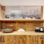 Holzvertäfelte Wand mit Waschbecken und Bergbild. Kaffeebereiter und Handtücher auf Arbeitsfläche.