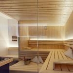 Sauna mit Holzbank, Steine und Kissen. Glaswand und Holzwände.