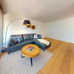 Wohnzimmer mit grauem Sofa, runden Tisch und Holzboden.