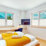 Schlafzimmer mit Bett, TV und zwei Fenstern mit Bergblick.
