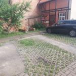 Vorhof mit gepflastertem Bereich, einem Baum und einem parkenden Auto.