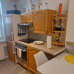 Küche mit Holzschränken, Kühlschrank, Herd und Esstisch mit Blumen.
