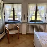 Bedroom with bed, chair, and two windows with curtains.
