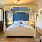 Bedroom with four-poster bed, blue wall, and wooden floor.