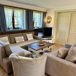 Living room with sofa, couch, and TV. Windows with curtains and wooden table.