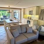 Living and dining area with kitchen, sofa, and armchair. Passage to terrace with garden view.