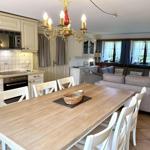 Dining area with table and chairs, kitchen, and living area with sofa and windows.