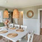 Dining room with white table, chairs, and rattan lamps. Hallway to bedroom with bed.