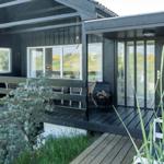Black house with terrace and glass doors. Garden with plants and wooden steps.
