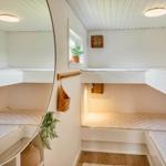 Two bunk beds with mattresses and pillows in a bright room with wooden floor and window.