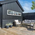 Deck with seating group, wooden floor, and black siding. Plants and tree in background.