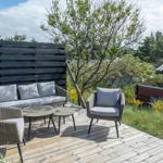 Deck with seating group, table, and wooden railing. Background: greenery and fence.
