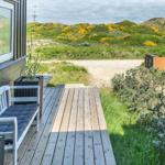 Deck with white chair and wooden floor. View of green hills with yellow flowers.