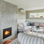 Living room with fireplace, sofa, and table. Windows and wainscoting visible.