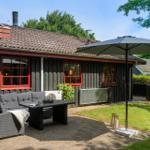 Terrace with seating, sunshade, and lawn in front of a house with red window frames.
