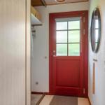 Red door with glass pane, mirror, and coat rack in hallway.