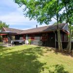 Wooden house with red window frames, terrace, and garden under trees.