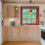 Kitchen with wooden cabinets, red window frame, and view of greenery.