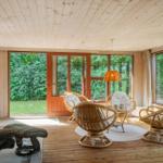 Living room with wooden ceiling, rattan chairs, and view of green garden.