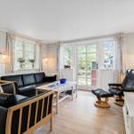 Living room with black leather furniture, wooden floor, and windows with curtains.