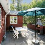 Terrace with table, chairs, umbrella, and grill. Background: forest and red wood walls.