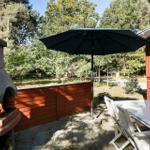 Terrace with grill, table, and umbrella beside red wooden house.
