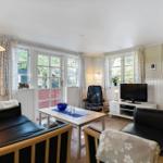 Living room with two black sofas, coffee table, and TV. Windows with curtains and wooden floor.