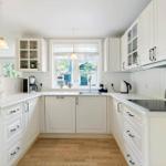 A white kitchen with wooden floor and window above the sink.
