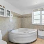 Bathroom with whirlpool, toilet, and window with roller blind.