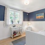 Bedroom with blue walls, white wainscoting, and wooden floor. Window with curtains, bed, and nightstand.