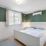 Bedroom with white bed, green walls and wooden floor. Window with curtains and nightstands.