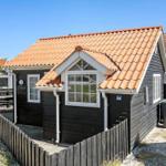 Black wooden house with red tiled roof and white-framed windows behind wooden fence.