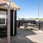 Terrace with table and benches, surrounded by wooden railing and view of houses.