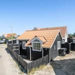 A small house with a red roof and black facade stands on a road.